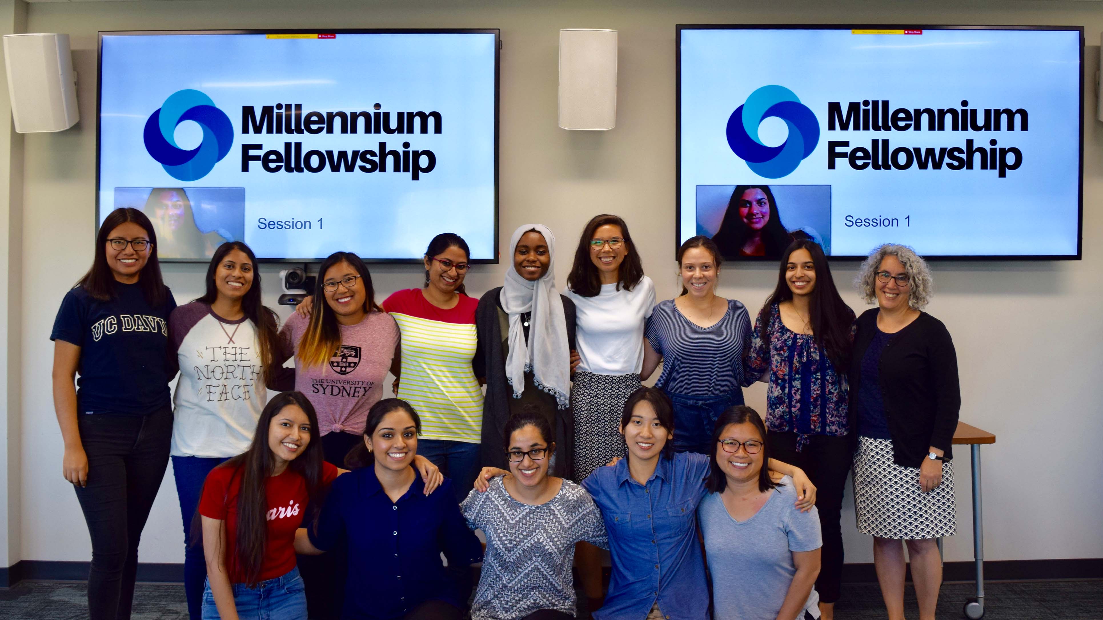A group of students standing in front of two large conference room TV screens. On both screens: a image of the UN Millennium Fellowship program.