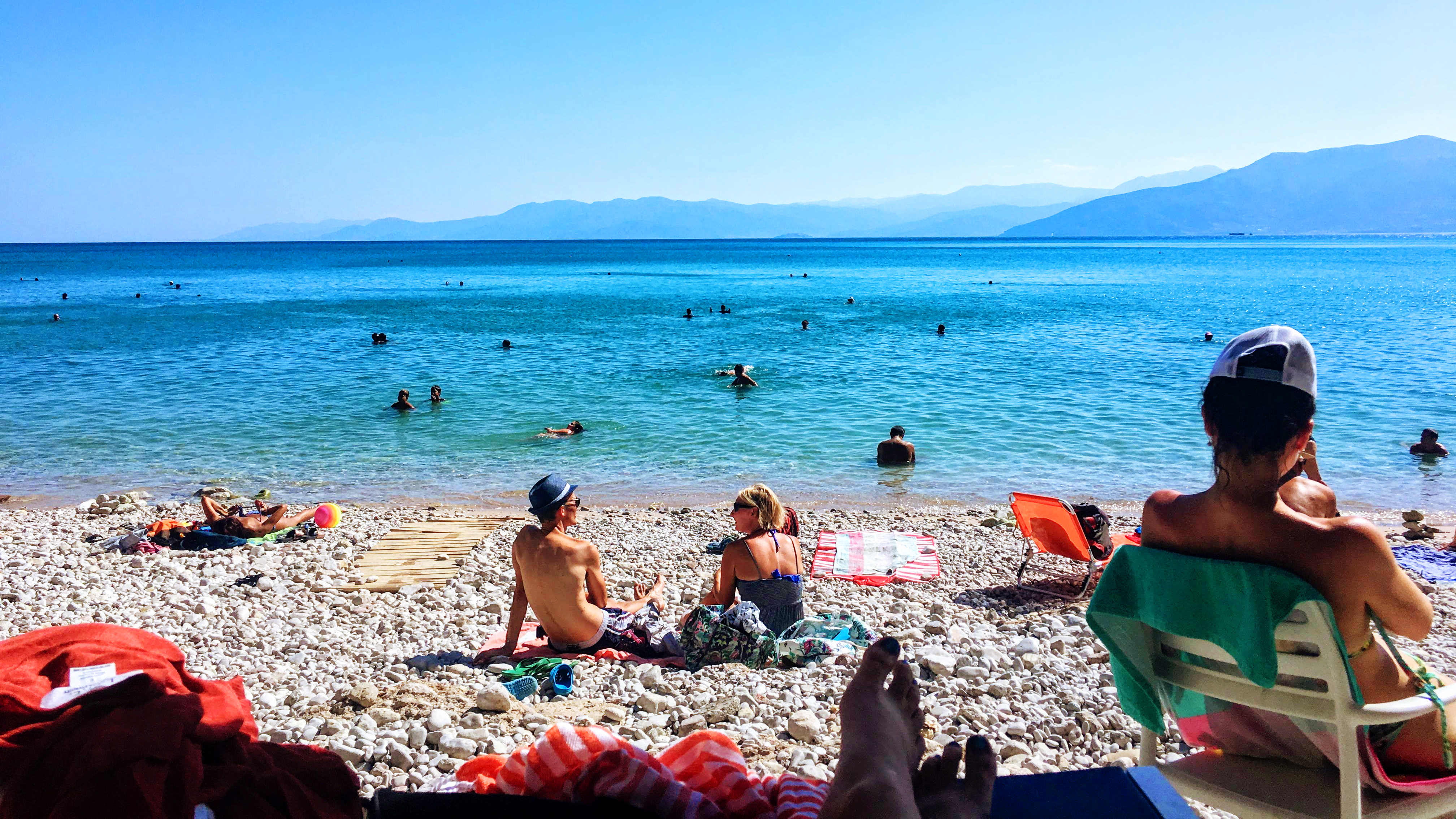 People lounge on a rocky beach in Nafplio, Greece