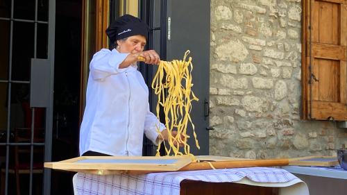 Photo of a women in Italy cooking a large amount of pasta. She is standing outside showing the participants on the study abroad program how to cook an authentic dish.