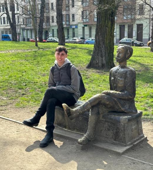 A photo of a student posing in a park next to a statue.